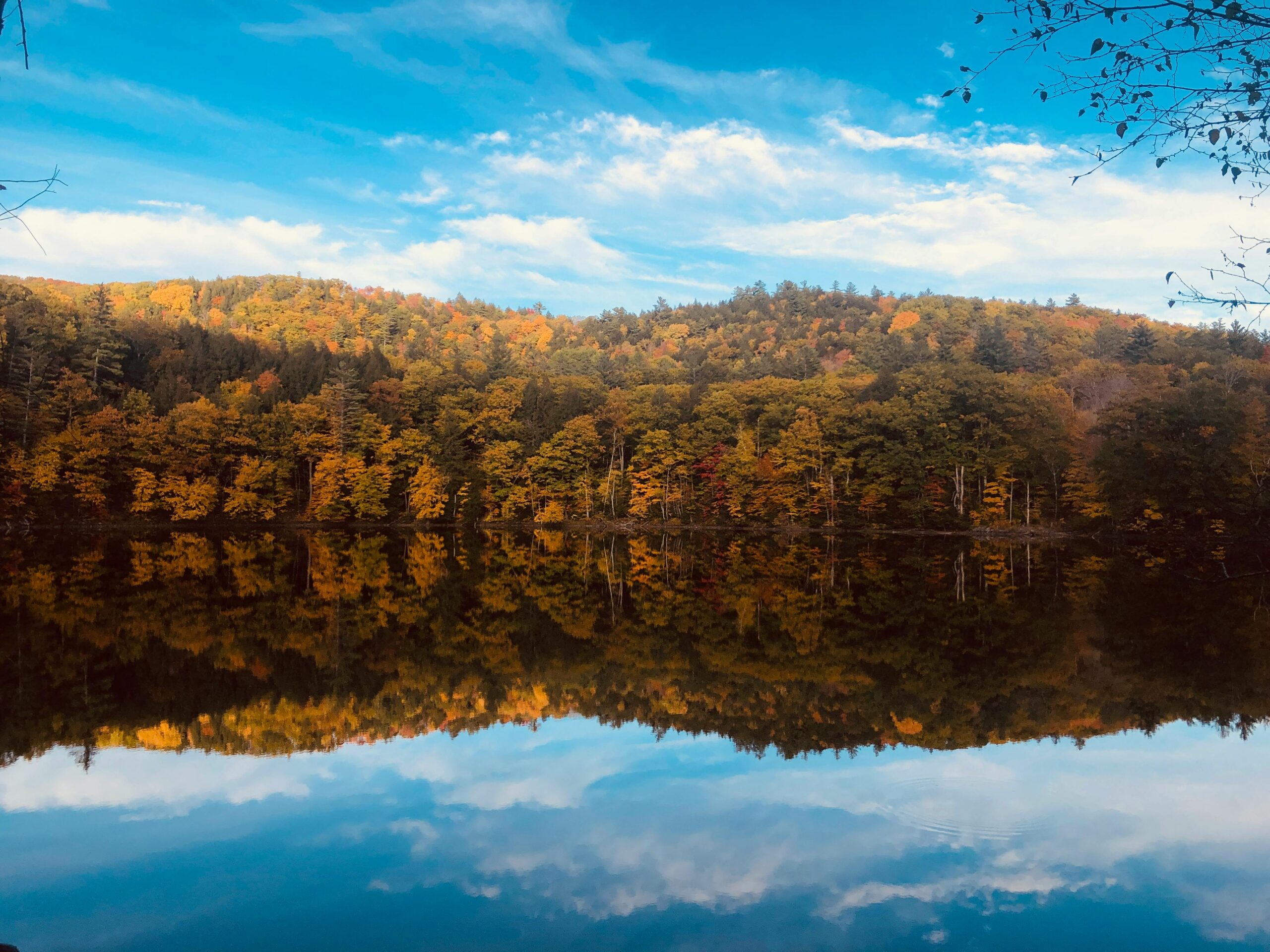 Beautiful autumn foliage reflected in a tranquil lake with a clear blue sky in Vermont.